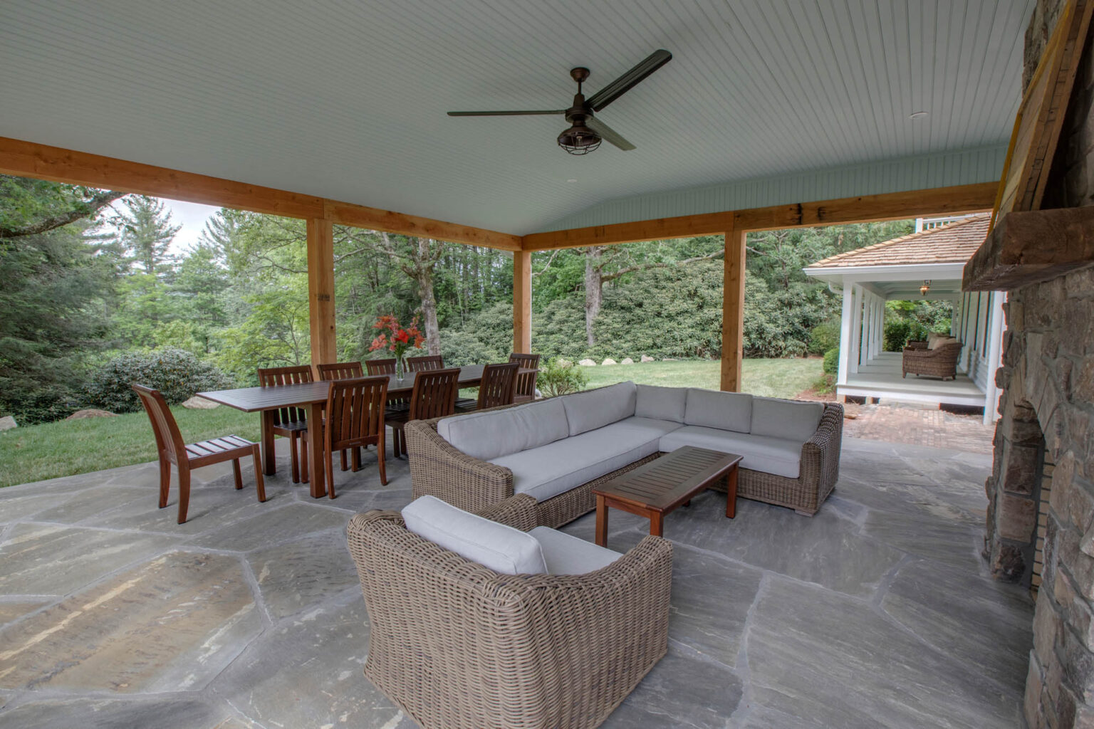 Covered stone patio with sofas, dining table and outdoor fireplace