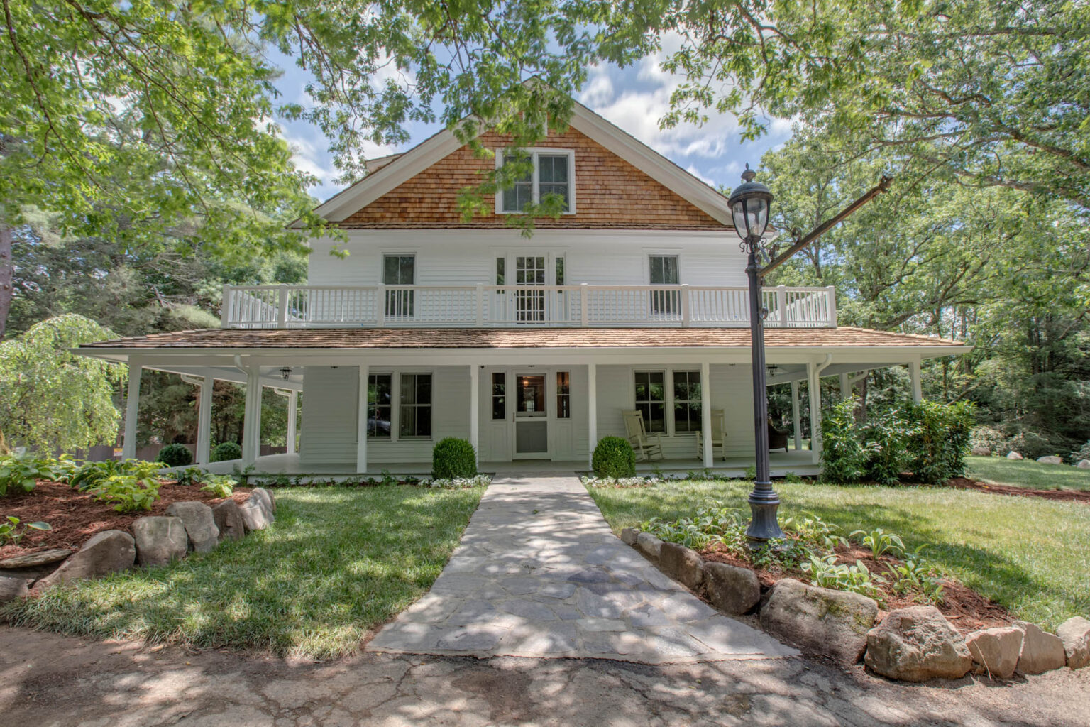 Fairview House, a white 1910 home with a wraparound porch and stone walkway, in summer