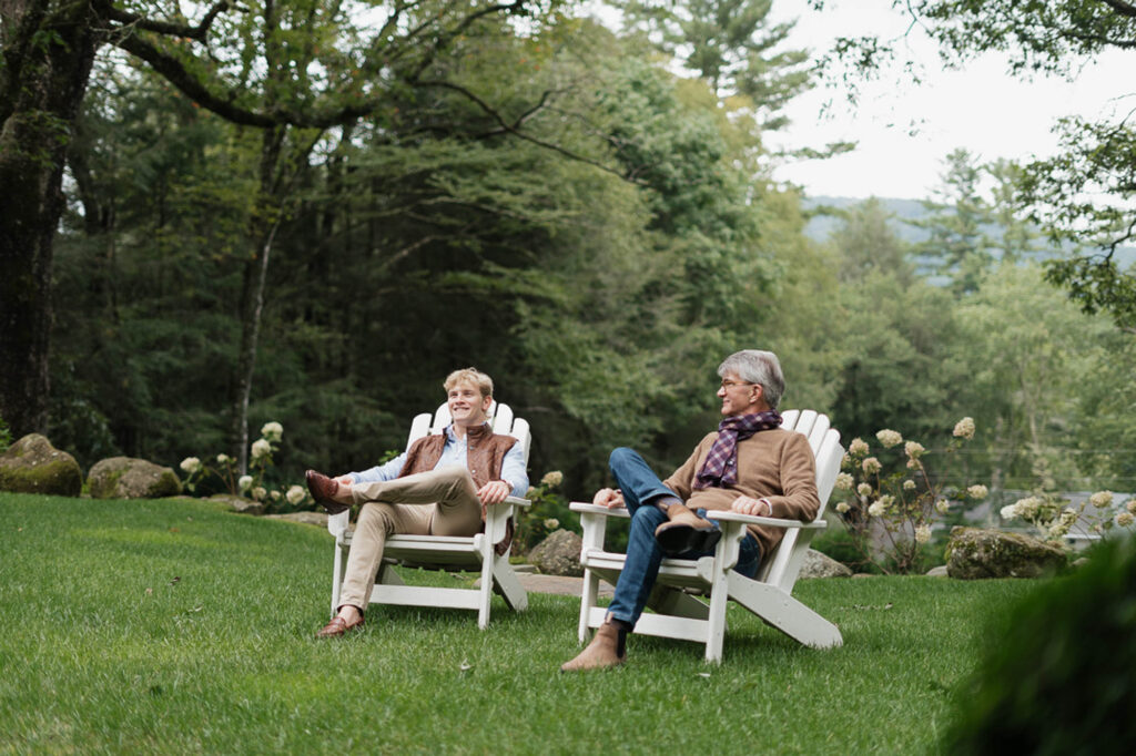 Two guests in Adirondack chairs on the lawn with forest behind